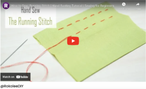 A person comparing their body measurements written on a notepad to a sewing pattern's size chart.